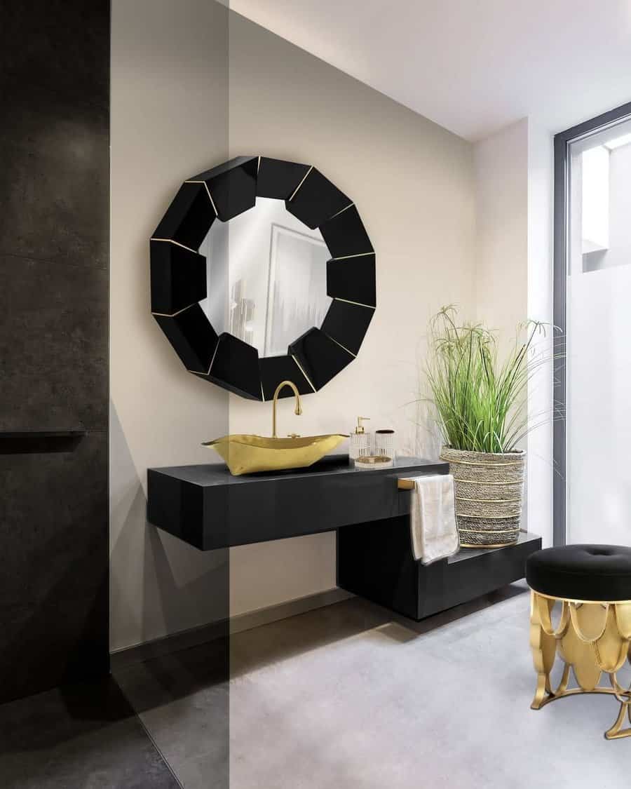 Modern bathroom with a geometric mirror, black floating vanity, gold faucet, plant in a large pot, and a black and gold stool