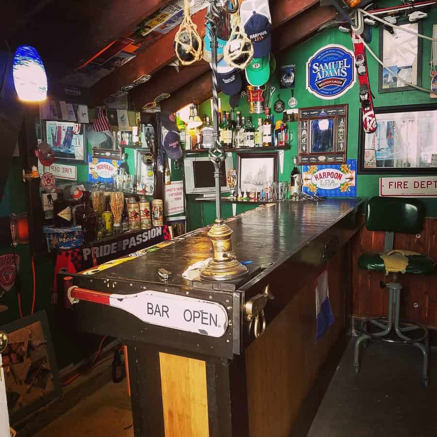 Cozy home bar with wooden counters, vintage signs, memorabilia, and assorted bottles, with a "Bar Open" sign displayed prominently