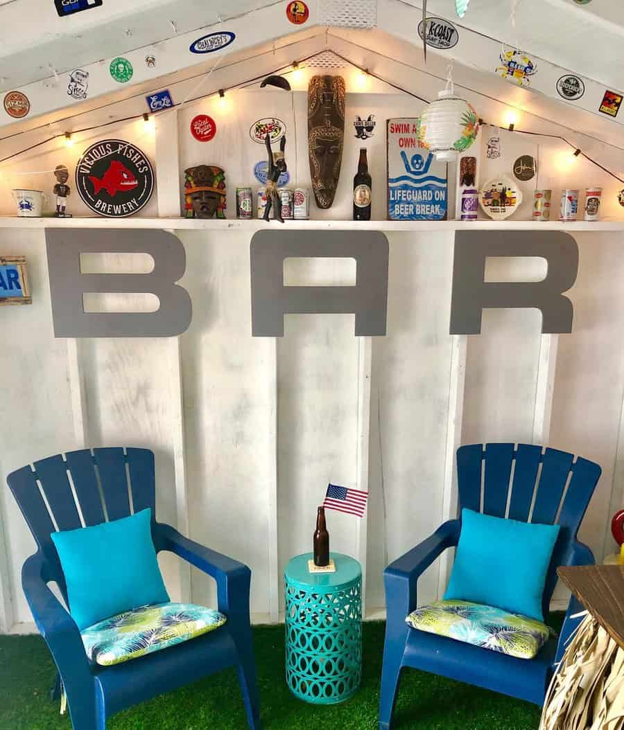 Cozy bar setup with two blue chairs, small table holding an American flag, and decorative wall items under string lights