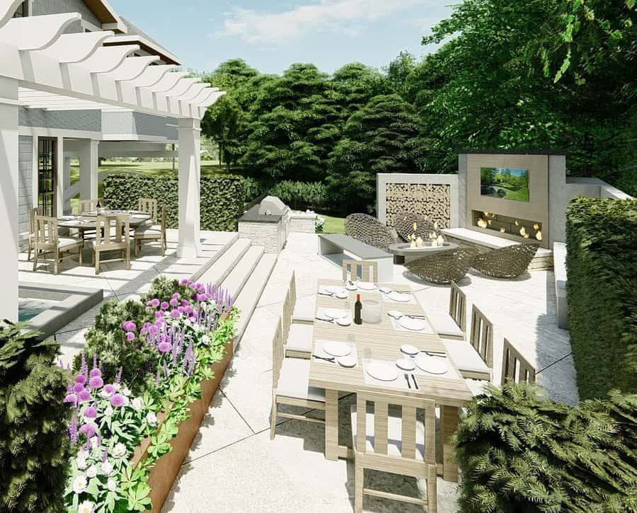 Outdoor patio with a pergola, dining tables, flowers, and a modern fireplace surrounded by greenery on a sunny day