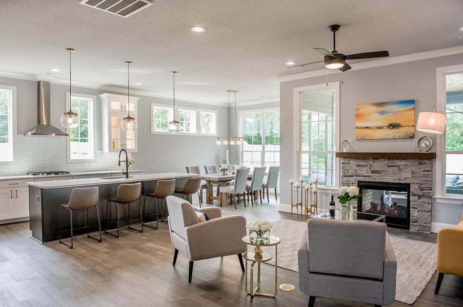 Open-concept living area with modern kitchen, dining table, and cozy seating by a stone fireplace, pendant lights hang above the kitchen island