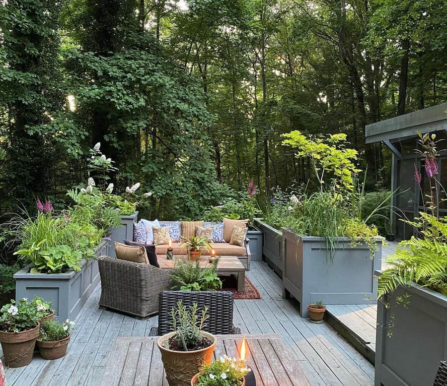 A cozy deck with wicker furniture, surrounded by lush planters and tall trees, creating a peaceful garden retreat