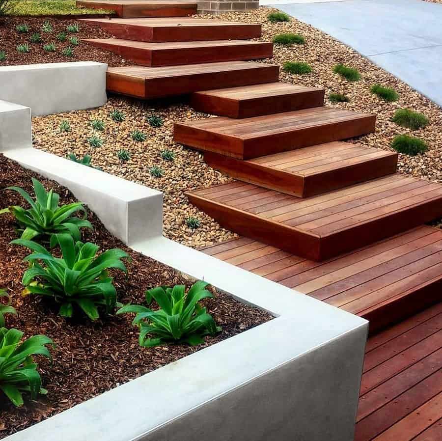 Modern terraced landscaping with wooden steps, gravel beds, neatly planted succulents, and concrete borders for a clean, layered look