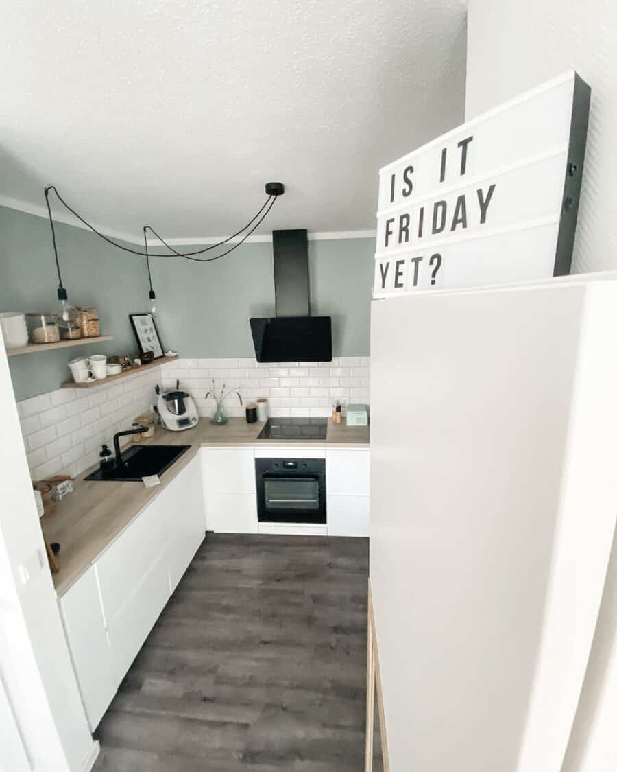 Modern small kitchen with white cabinets, open shelving, subway tile backsplash, and a lightbox sign reading 'Is it Friday yet?'