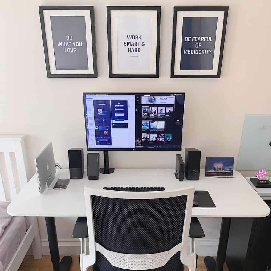 Minimalist home office with a PC, laptop, keyboard, and speakers on a white desk; three motivational posters hang above the monitor