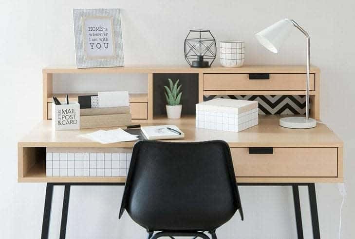 Wooden desk with black chair, lamp, plant, decor items, and stationary. Framed quote says, "Home is Wherever I'm with You"