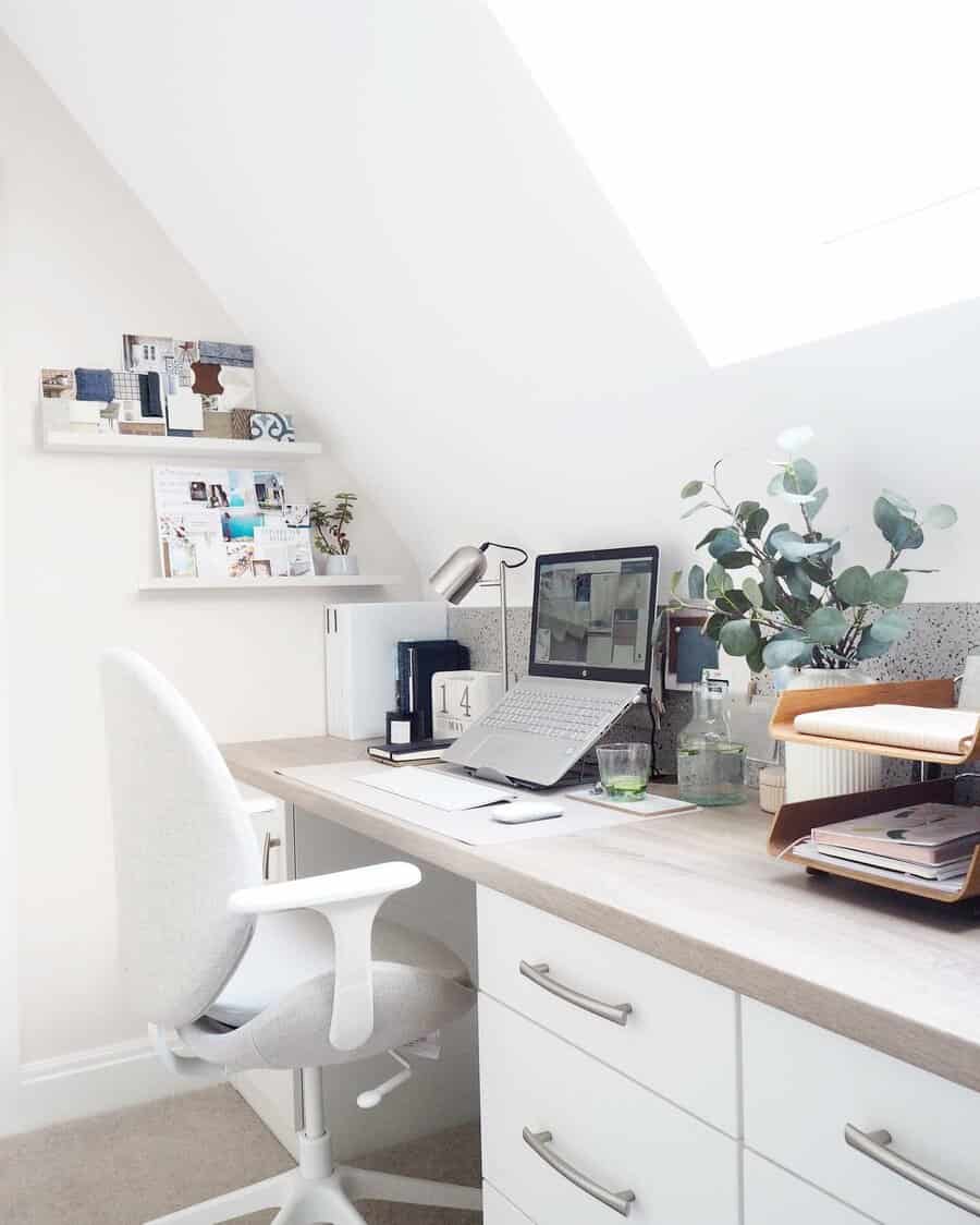 Bright home office with a desk under a skylight, featuring a laptop, chair, plants, lamp, and organized office supplies