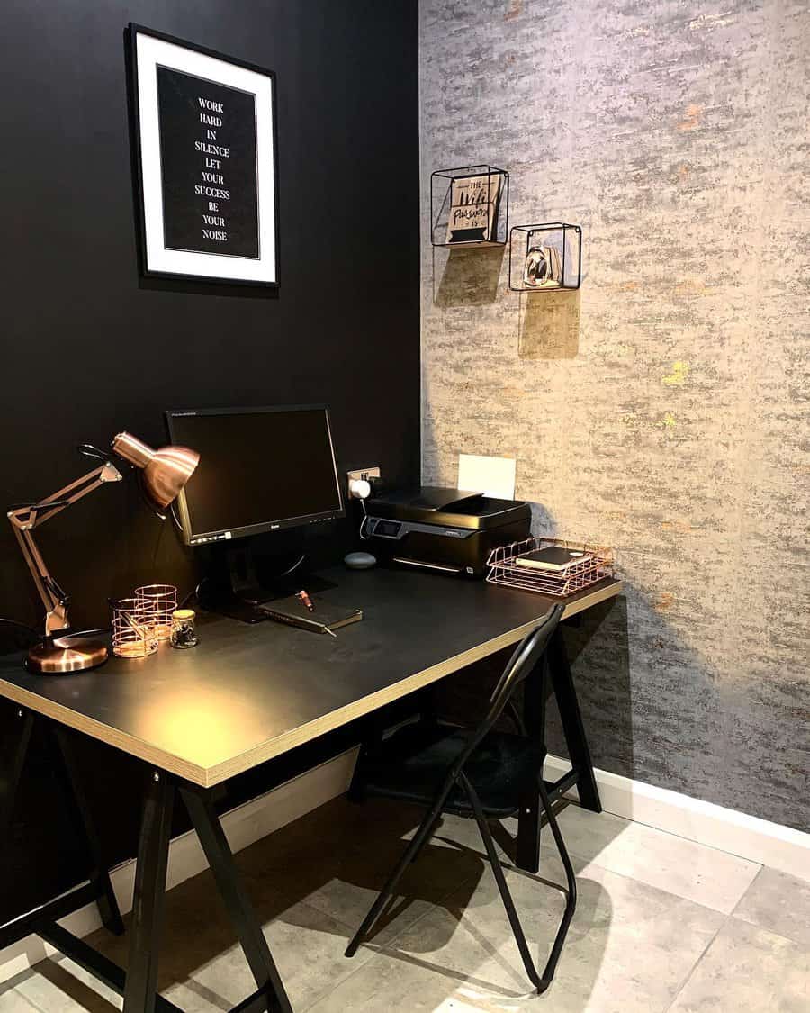 A modern home office with a black desk, chair, computer, desk lamp, and wall decor, featuring grey textured and black walls for added contrast