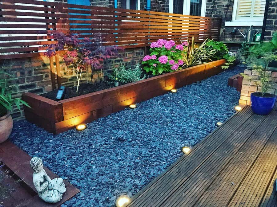 Cozy backyard with slate gravel, wooden planters, vibrant hydrangeas, ambient lighting, and a wooden deck with a serene Buddha statue