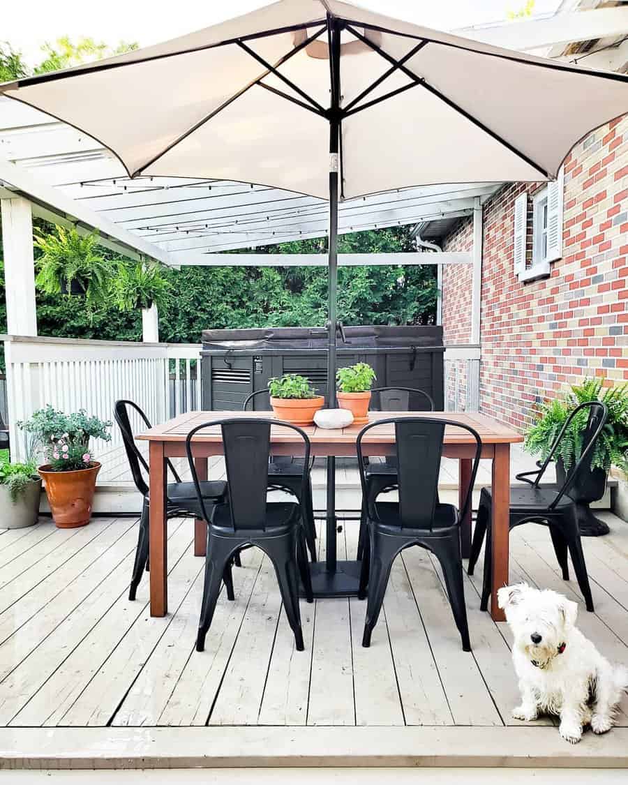 Outdoor patio deck with a wooden table, six black chairs, potted plants, and a large umbrella