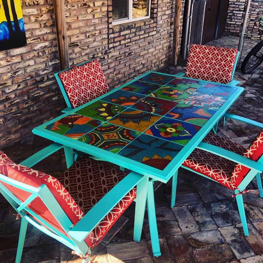 Colorful outdoor table with vibrant mosaic design and four red patterned chairs on a brick patio