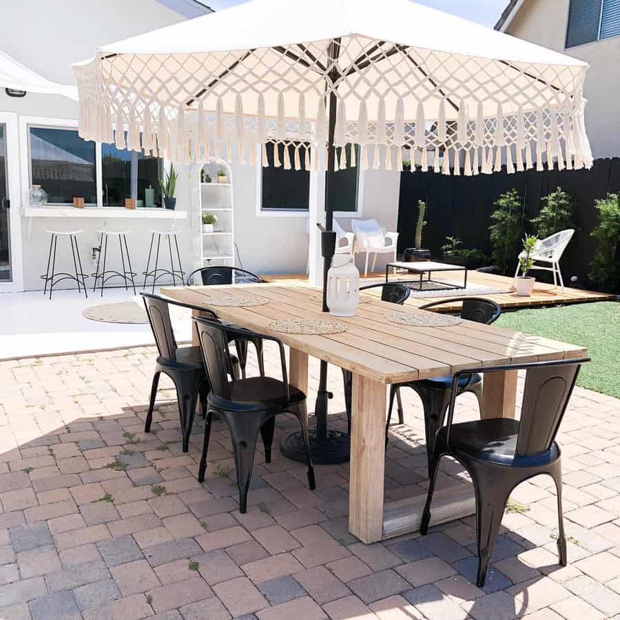 Outdoor patio with a wooden table, black chairs, and a large umbrella. Nearby, a bar area and seating with green artificial grass