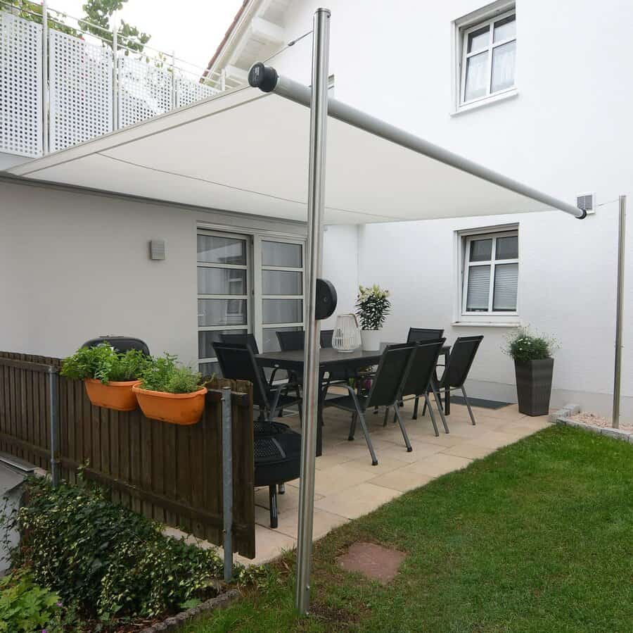 A patio with a retractable awning, table with chairs, potted plants, and a small garden by a white house