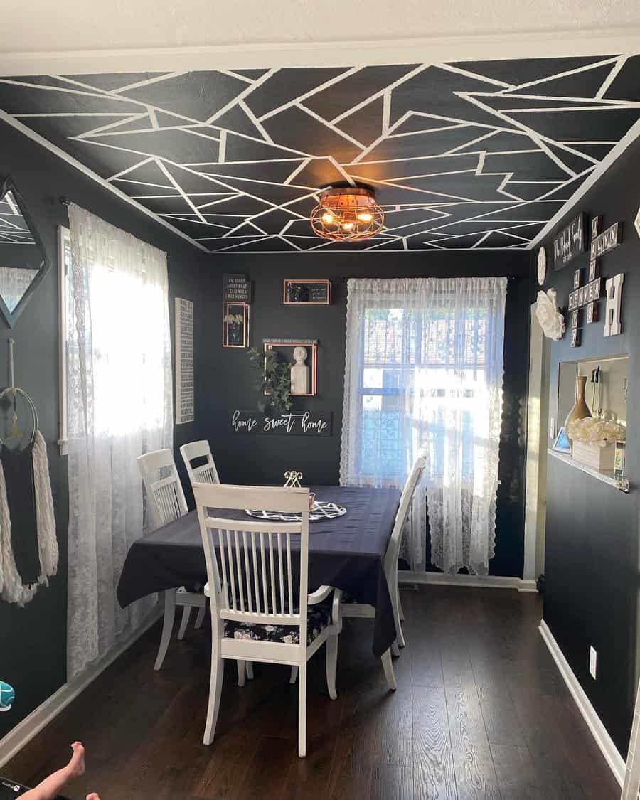 Dining room with geometric ceiling design, dark walls, white curtains, and a table with chairs featuring wall decor including photos and signs