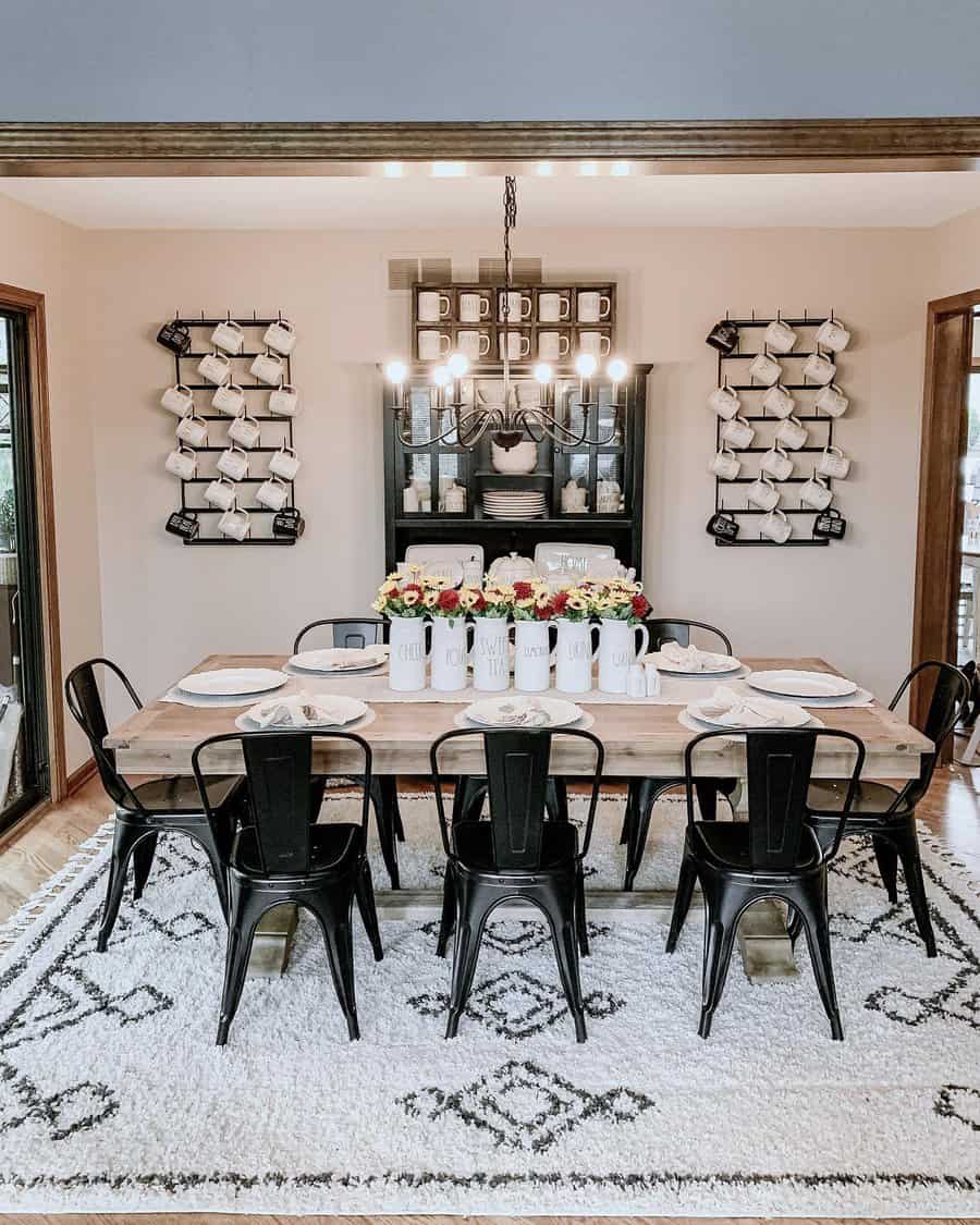 Dining room with a wooden table, black chairs, and hanging light. Wall decor features metal racks with cups and plates