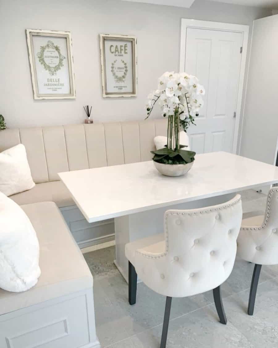 Chic dining area with white table, tufted chairs, corner bench, and potted white orchids; framed art decorates the wall