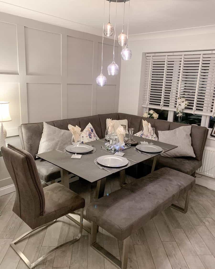 Modern dining area with a gray corner sofa, a rectangular table set for four, and pendant lights above, neutral tones dominate the decor