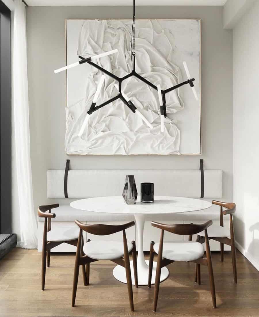 Modern dining area with a white round table, four chairs, abstract wall art, and a geometric chandelier above; wood floor and neutral tones