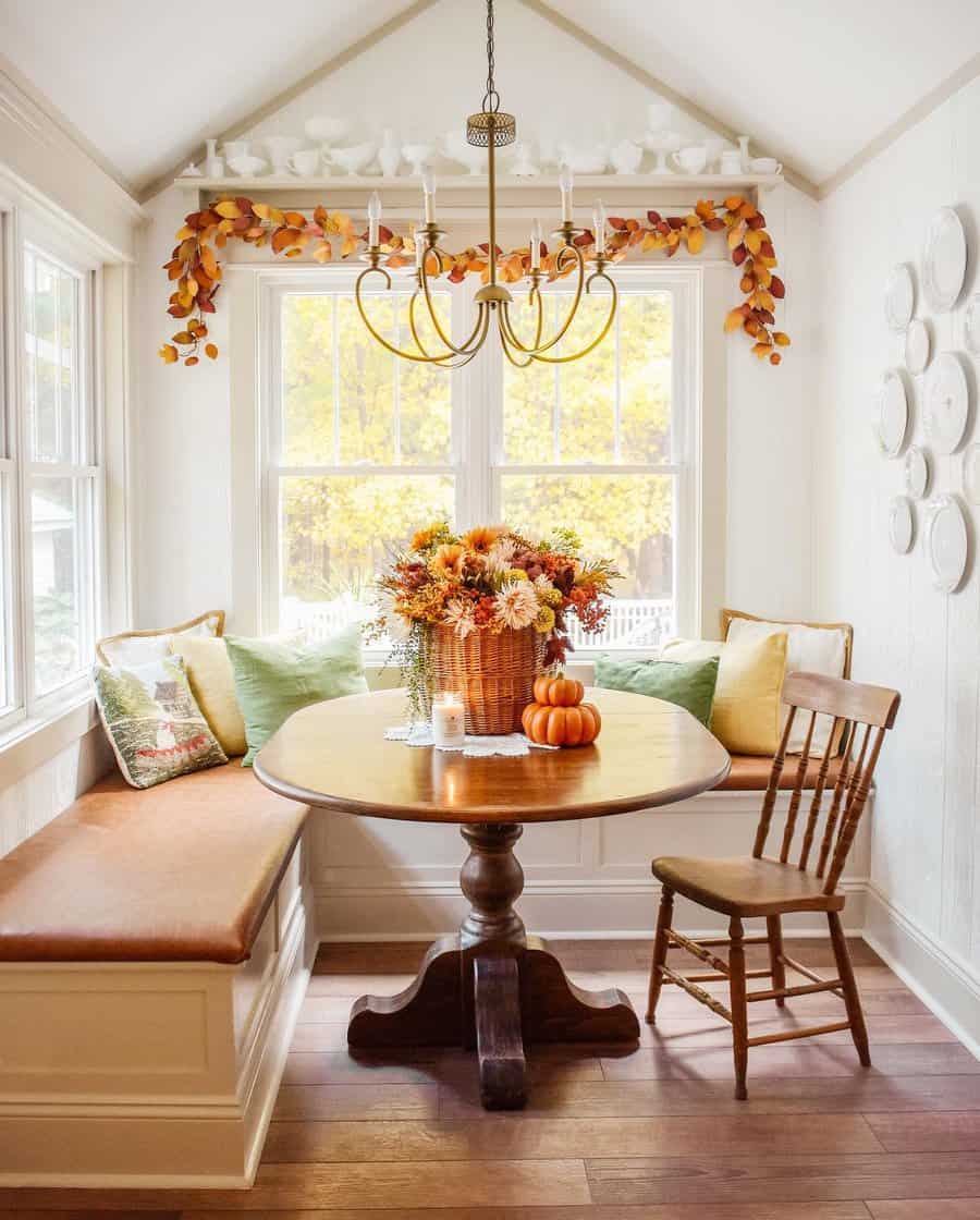 Cozy dining nook with autumn decor, featuring a round table, wooden chair, bench seating, and seasonal flowers and pumpkins