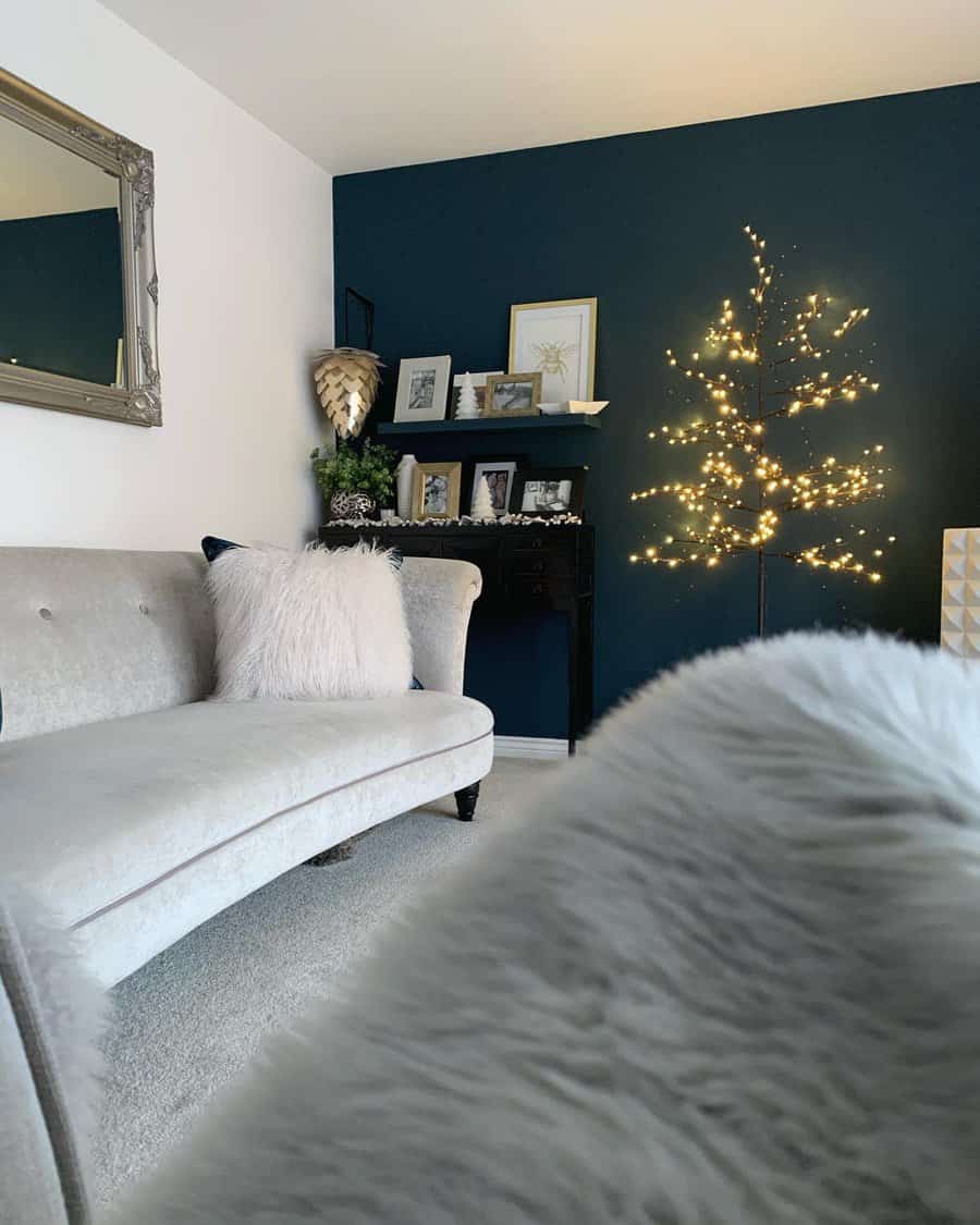 Cozy living room with a light gray sofa, fluffy cushions, and a lit decorative branch tree, dark accent wall with framed art