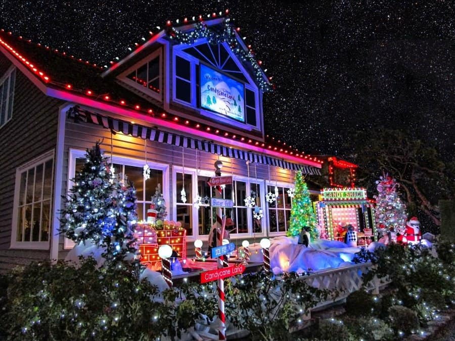 A house decorated with colorful Christmas lights, snowmen, and Santa figures under a starry night sky