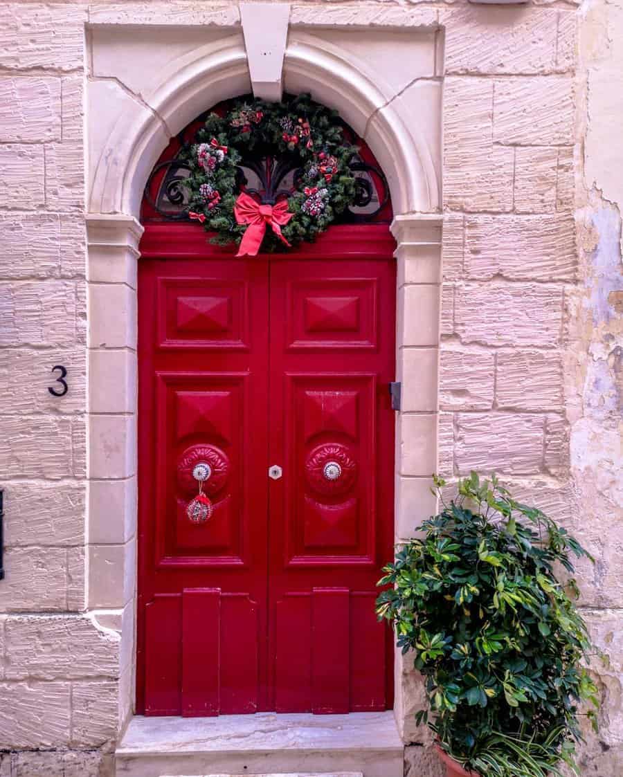 Red door with a Christmas wreath and a potted plant outside