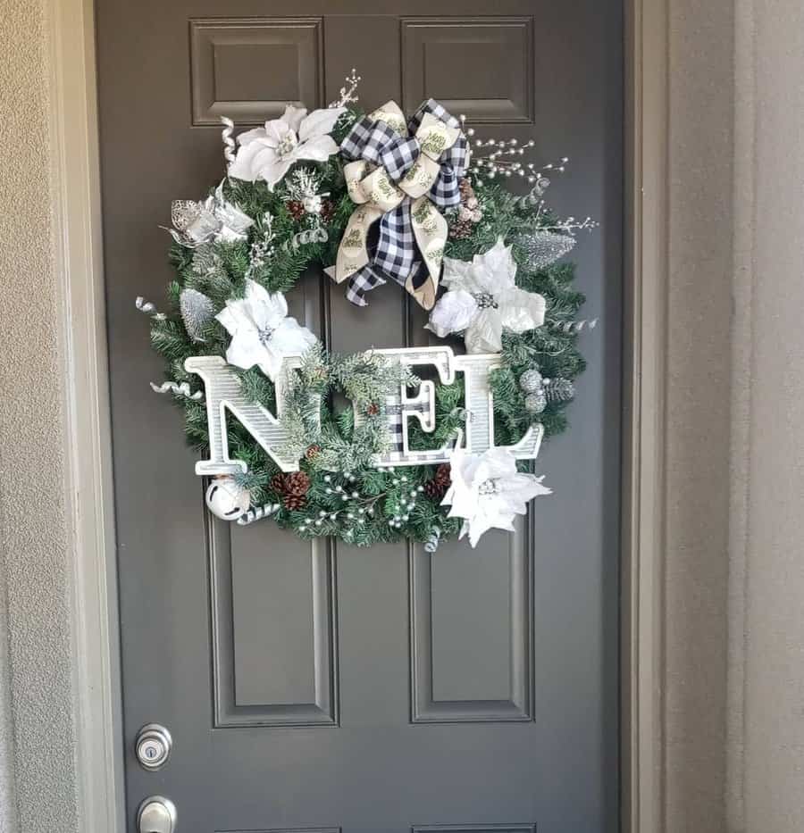 A Christmas wreath on a door with the word "NOEL" and white poinsettias