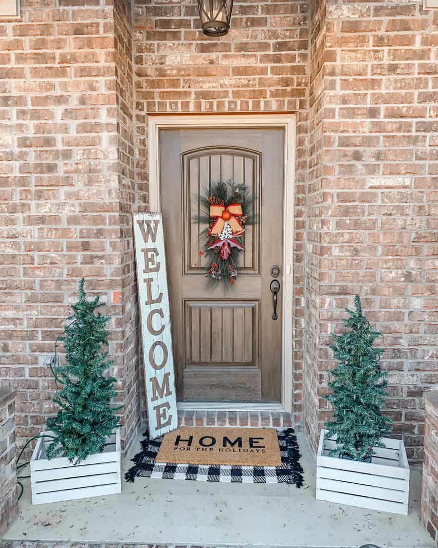 Front porch with holiday decor: wreath on door, welcome sign, and small Christmas trees