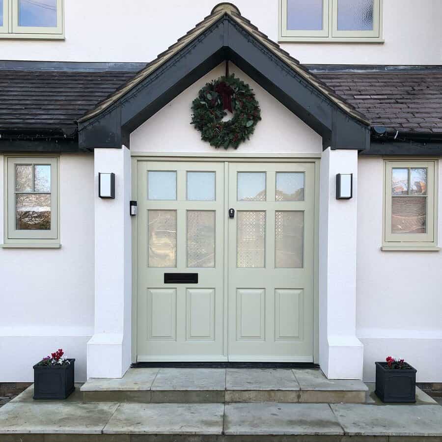 White house front with muted cream double front doors, a wreath above, and two potted plants on either side