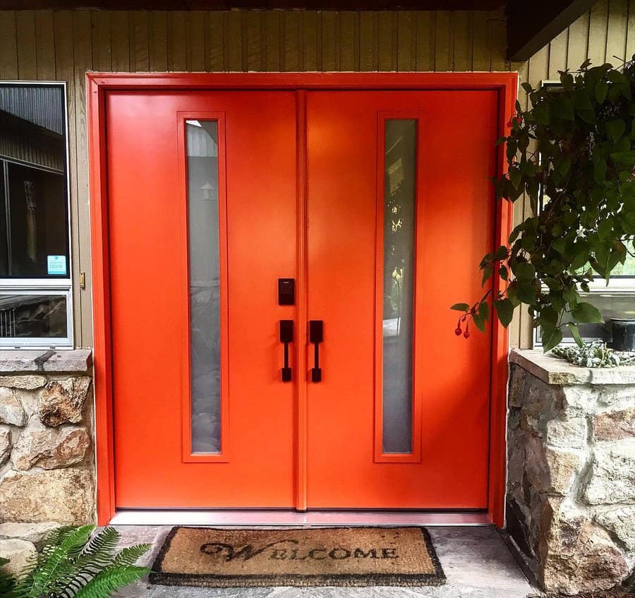 Bright red double doors with vertical glass panels, set in a stone wall A "Welcome" doormat lies at the base