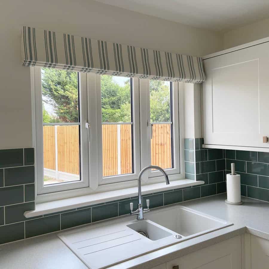 Modern kitchen with a white double sink, built-in drainboard, sleek chrome faucet, and green subway tile backsplash under a striped valance