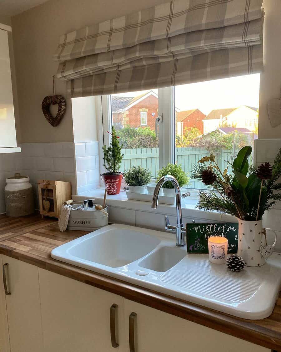 Cozy kitchen with a white sink and drainboard, wooden countertop, festive decor, and potted plants by the window for a warm holiday touch