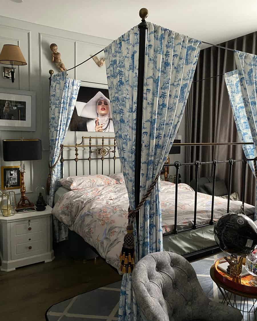 Elegant bedroom with a canopy bed, floral curtains, patterned bedding, wall art, a plush chair, and a vintage bedside table