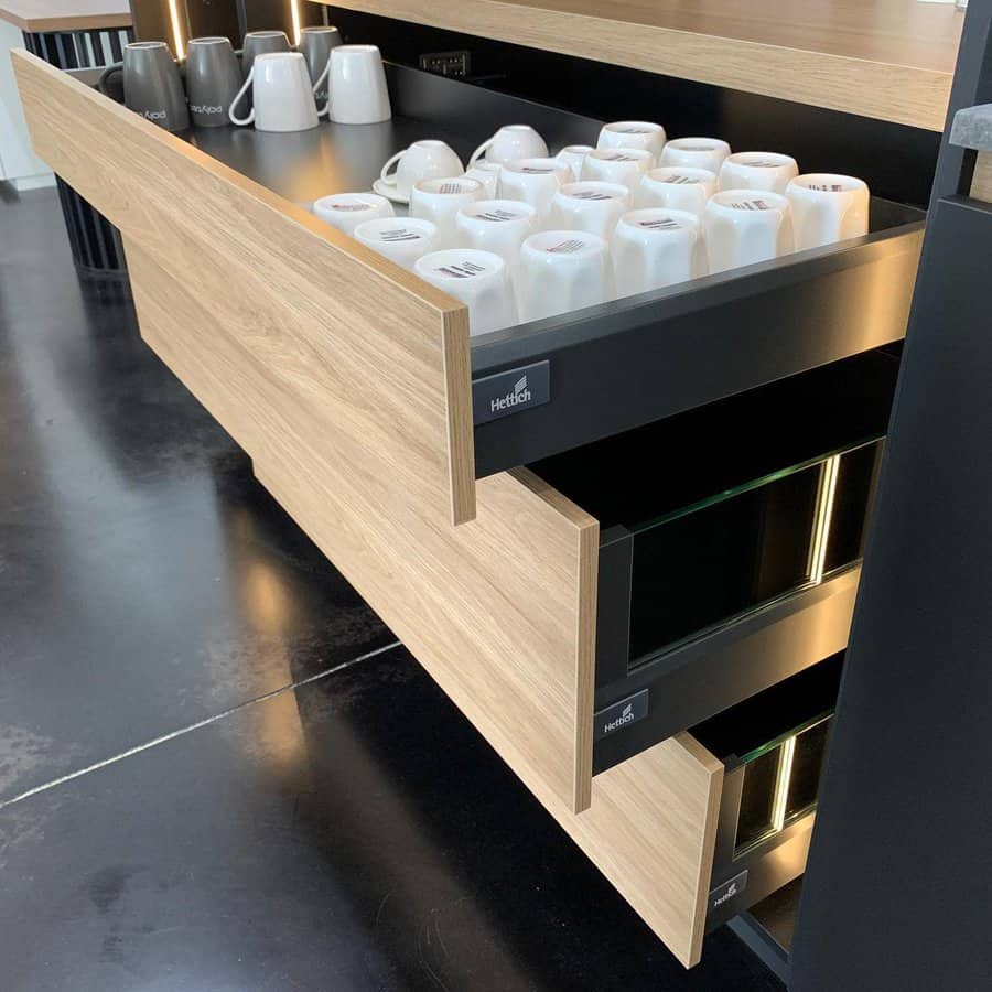 Modern kitchen with sleek wooden pull-out drawers, neatly organized coffee mugs, and hidden storage for an efficient and stylish design