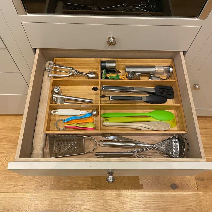 Neatly organized kitchen drawer with wooden dividers, storing utensils, graters, tongs, and colorful cooking tools for easy access