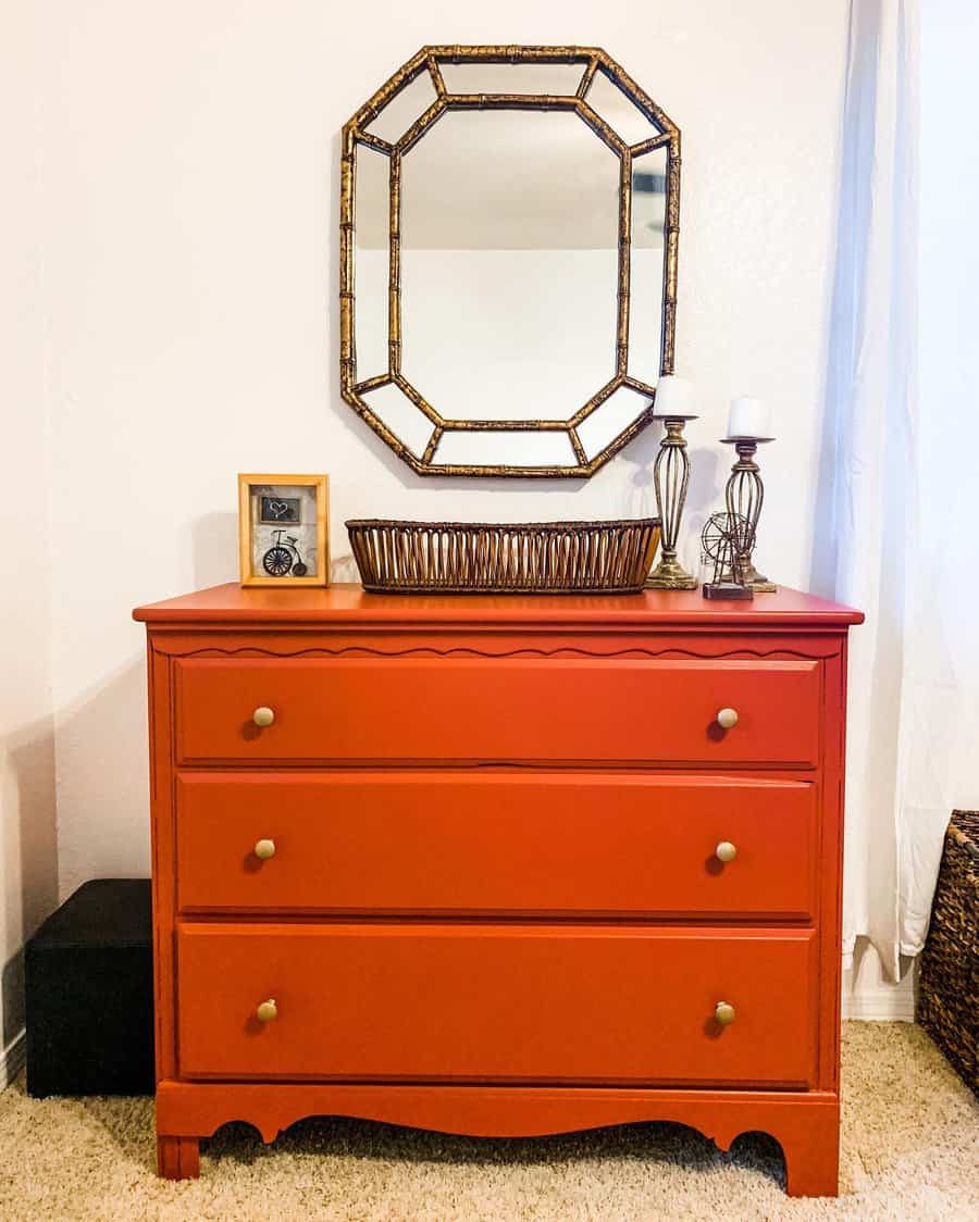 Bold red dresser with gold knobs, styled with a wicker basket, vintage decor, and a geometric gold mirror for a warm, elegant look.