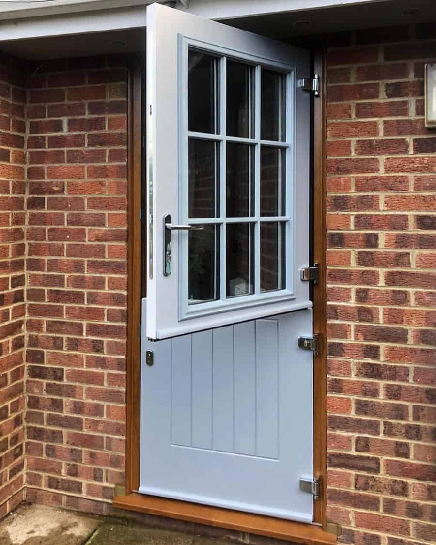 A partially open muted blue Dutch door with glass panes, set in a brick wall