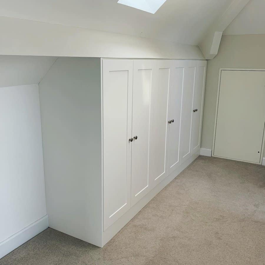 Built-in white wardrobes in an attic, maximizing storage space under the sloped ceiling with a clean and minimalist design.