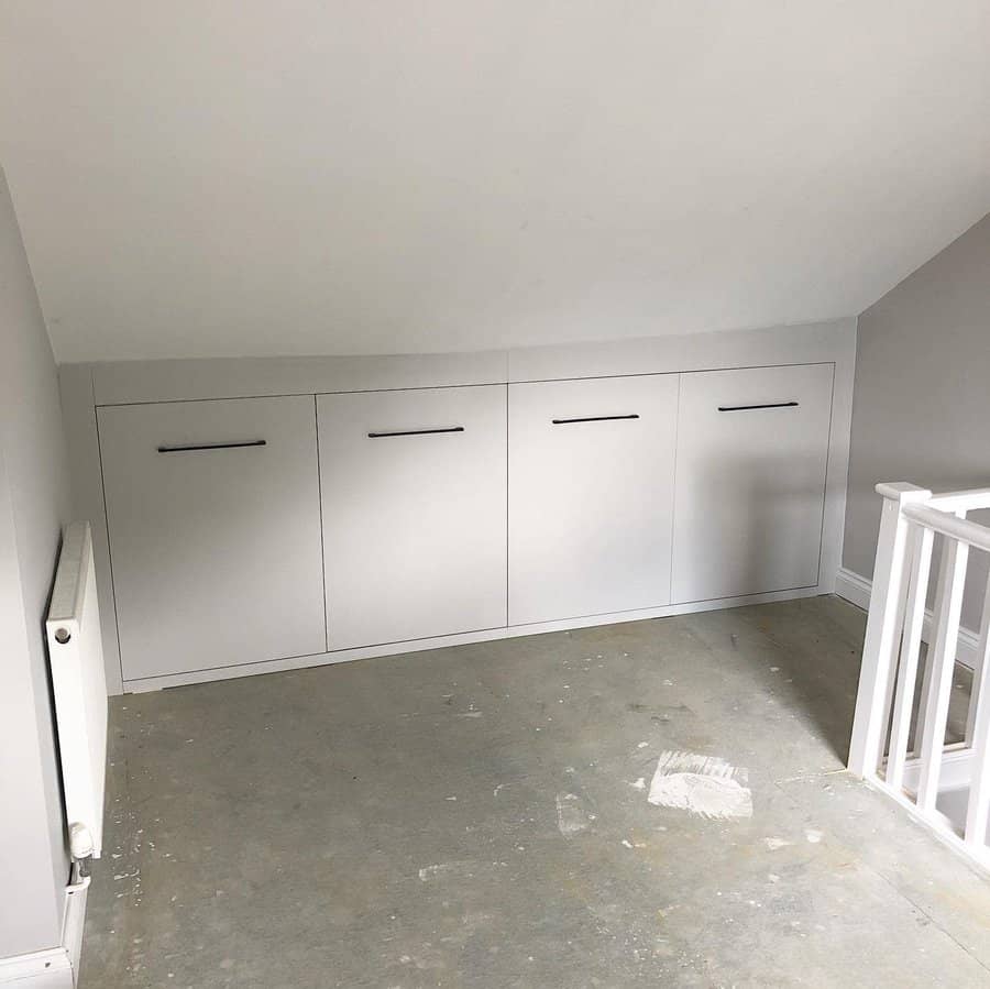 Sleek built-in white storage cabinets under a sloped attic ceiling, offering a minimalist and space-saving storage solution.