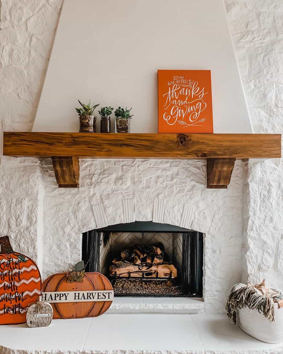 A cozy rustic fireplace mantel adorned with autumn-themed decor, including pumpkins, a gratitude sign, and potted plants for a festive look