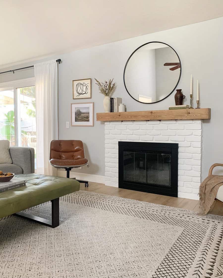 A minimalist white brick fireplace with a wooden mantel, complemented by a large round mirror, candles, and tasteful decor for a clean, modern look