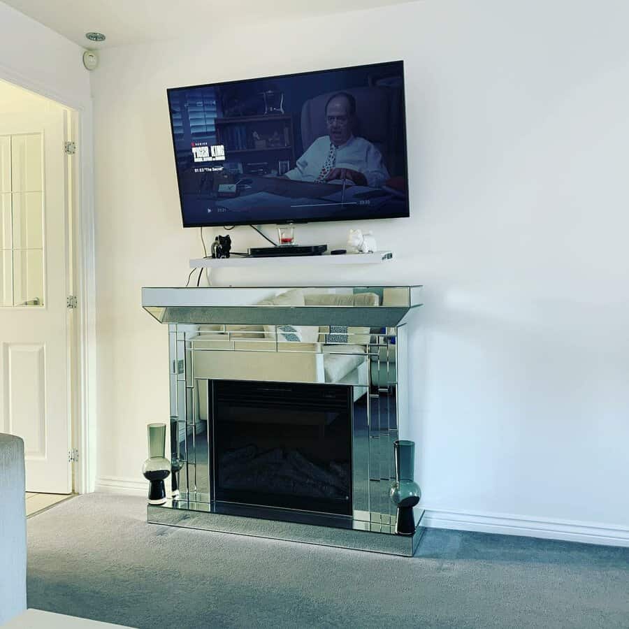 A sleek, mirrored fireplace mantel with a modern aesthetic, accompanied by a wall-mounted TV and minimalistic decor for a contemporary living space