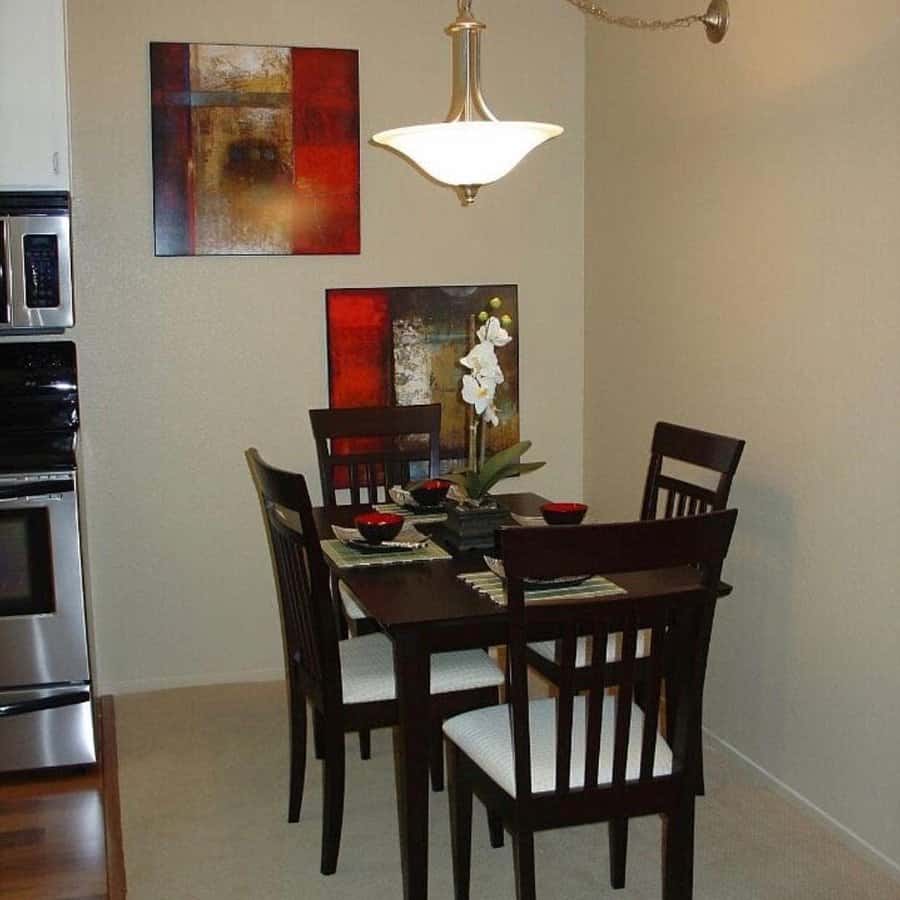 A small dining area featuring a dark wood table set for four, adorned with decorative red and brown wall art and a hanging light fixture