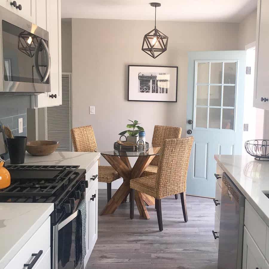 Modern kitchen with white cabinets, wood dining table, wicker chairs, and a geometric light fixture, blue door and wall art in background