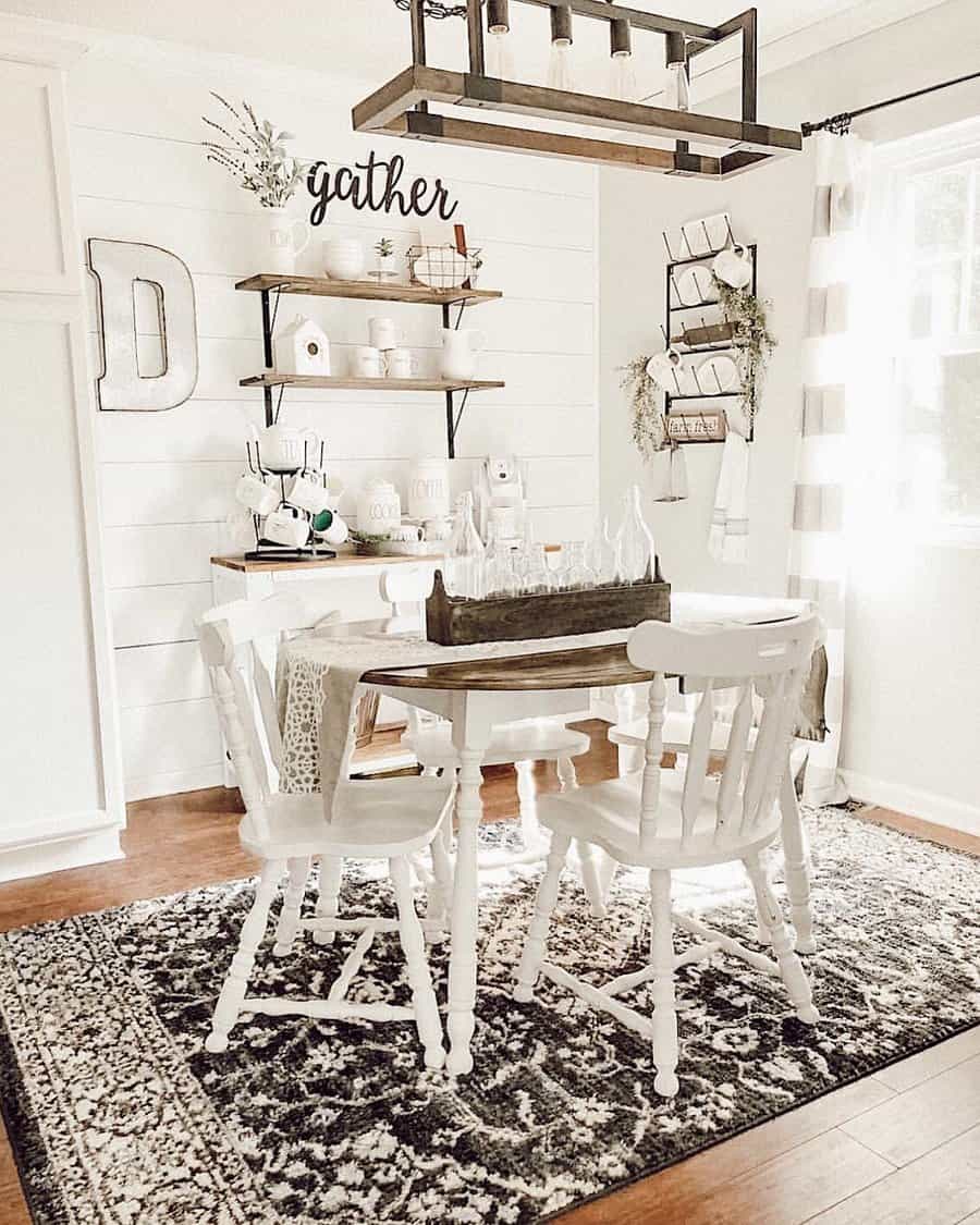 Farmhouse dining area with white table and chairs, rustic decor, shelves with mugs, and a decorative sign reading "gather