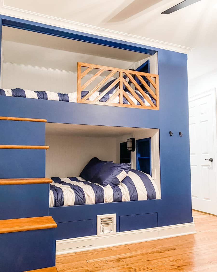 Blue bunk bed with striped bedding, wooden safety rail, adjacent wooden steps, and a small reading light in a bright room