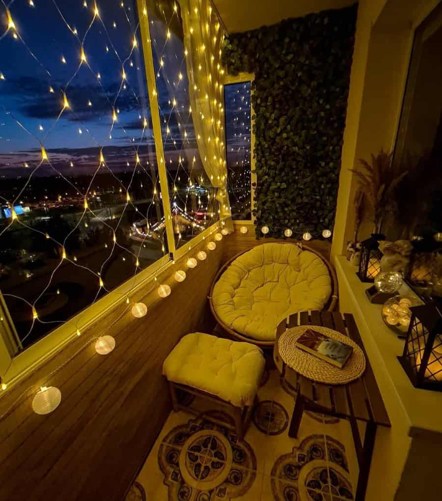 Cozy enclosed balcony at night with warm string lights, a papasan chair, a wooden table, lanterns, and a city view