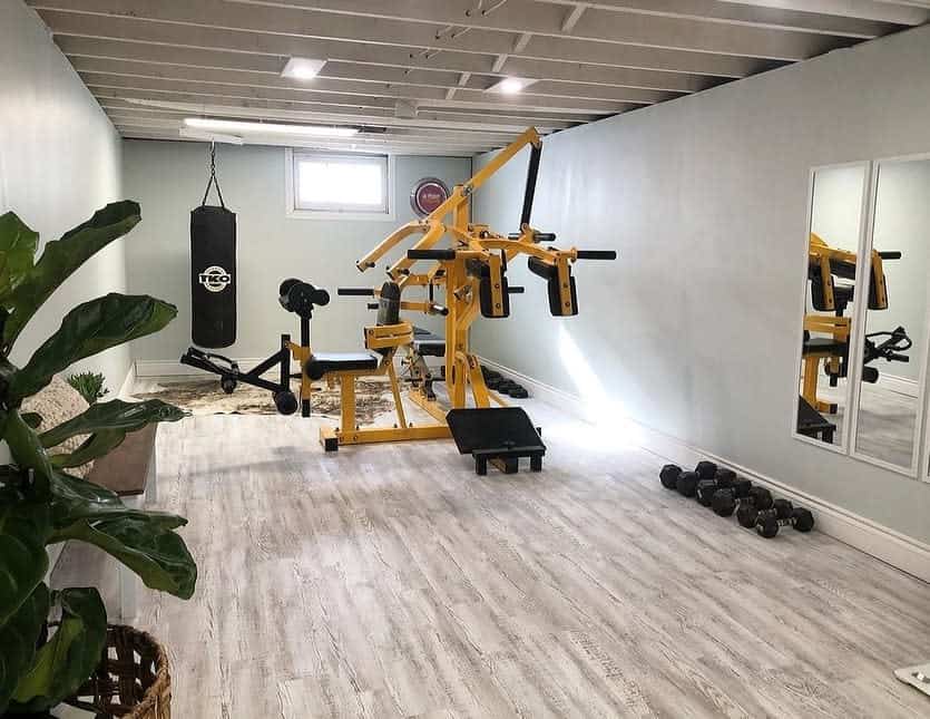 Modern basement home gym with an open ceiling, sleek flooring, a weightlifting station, punching bag, and mirrors for a dynamic workout space.