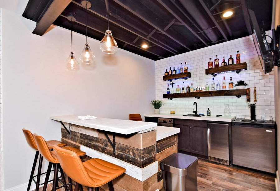 Industrial-style basement bar with an open black ceiling, rustic wood accents, leather barstools, and subway tile backsplash for a modern touch.