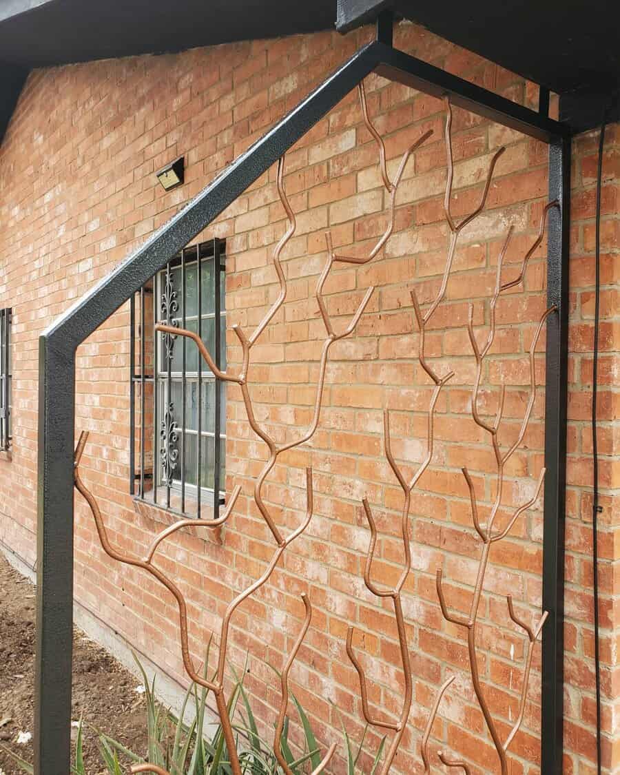 Wrought iron gate with tree branch design against a brick wall, small window with bars visible on the wall